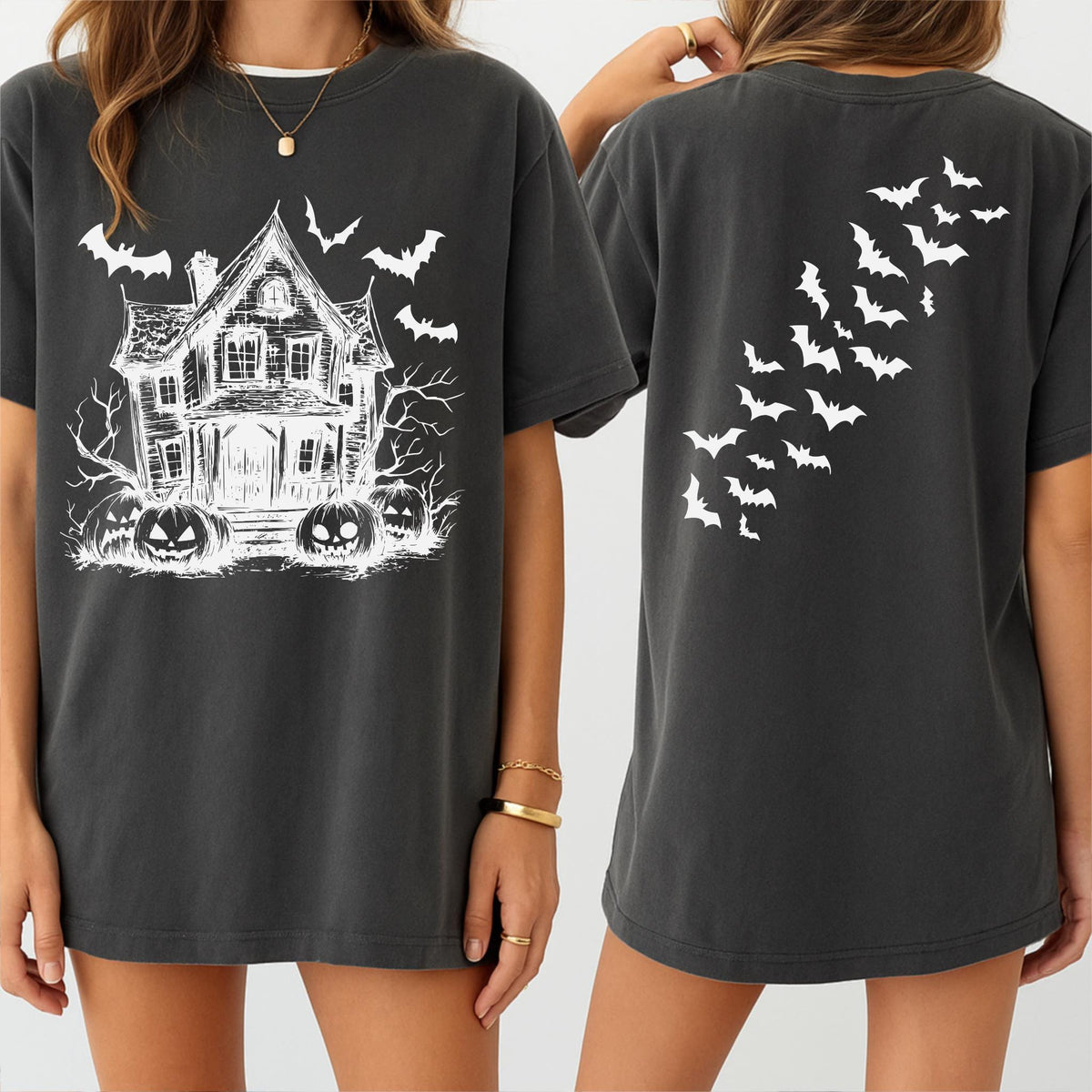 May include: Dark gray t-shirt featuring a white graphic of a haunted house, bats, and pumpkins. The back of the shirt displays a flock of white bats. The shirt is a comfortable, casual style, perfect for Halloween.