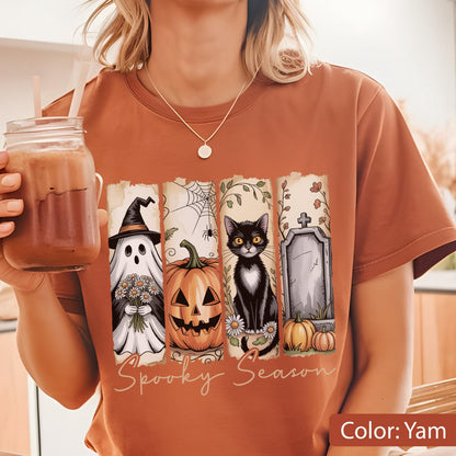 May include: A yam-colored t-shirt featuring a Halloween-themed design. The design includes a ghost, jack-o'-lantern, black cat, and tombstone, with the words "Spooky Season" below. The shirt is made of a soft material.