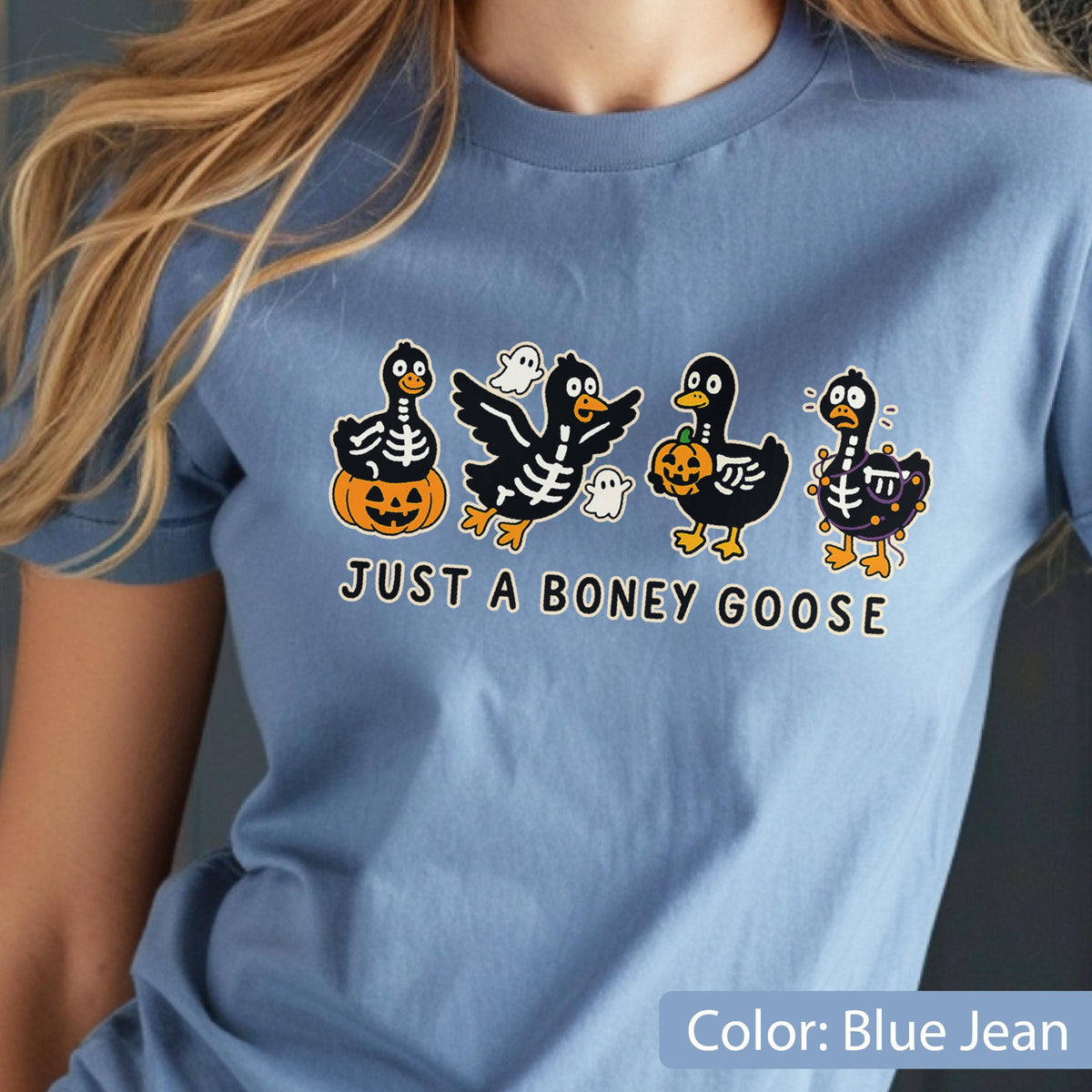 May include: A blue jean colored t-shirt featuring a Halloween-themed graphic. The graphic includes four cartoon geese with skeleton designs, pumpkins, and ghosts. The text "JUST A BONEY GOOSE" is printed below the geese.