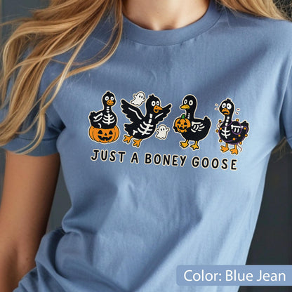 May include: A blue jean colored t-shirt featuring a Halloween-themed graphic. The graphic includes four cartoon geese with skeleton designs, pumpkins, and ghosts. The text "JUST A BONEY GOOSE" is printed below the geese.