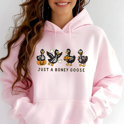 May include: A light pink hoodie with a graphic of four cartoon geese dressed as skeletons, holding pumpkins and a ghost. The text "JUST A BONEY GOOSE" is printed below the geese in white.