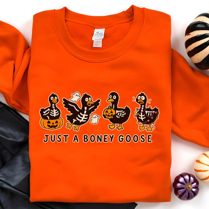 May include: Orange sweatshirt with a Halloween-themed graphic. The design features four cartoon geese in skeleton costumes, holding pumpkins and accompanied by ghosts. The text "JUST A BONEY GOOSE" is printed below the geese.