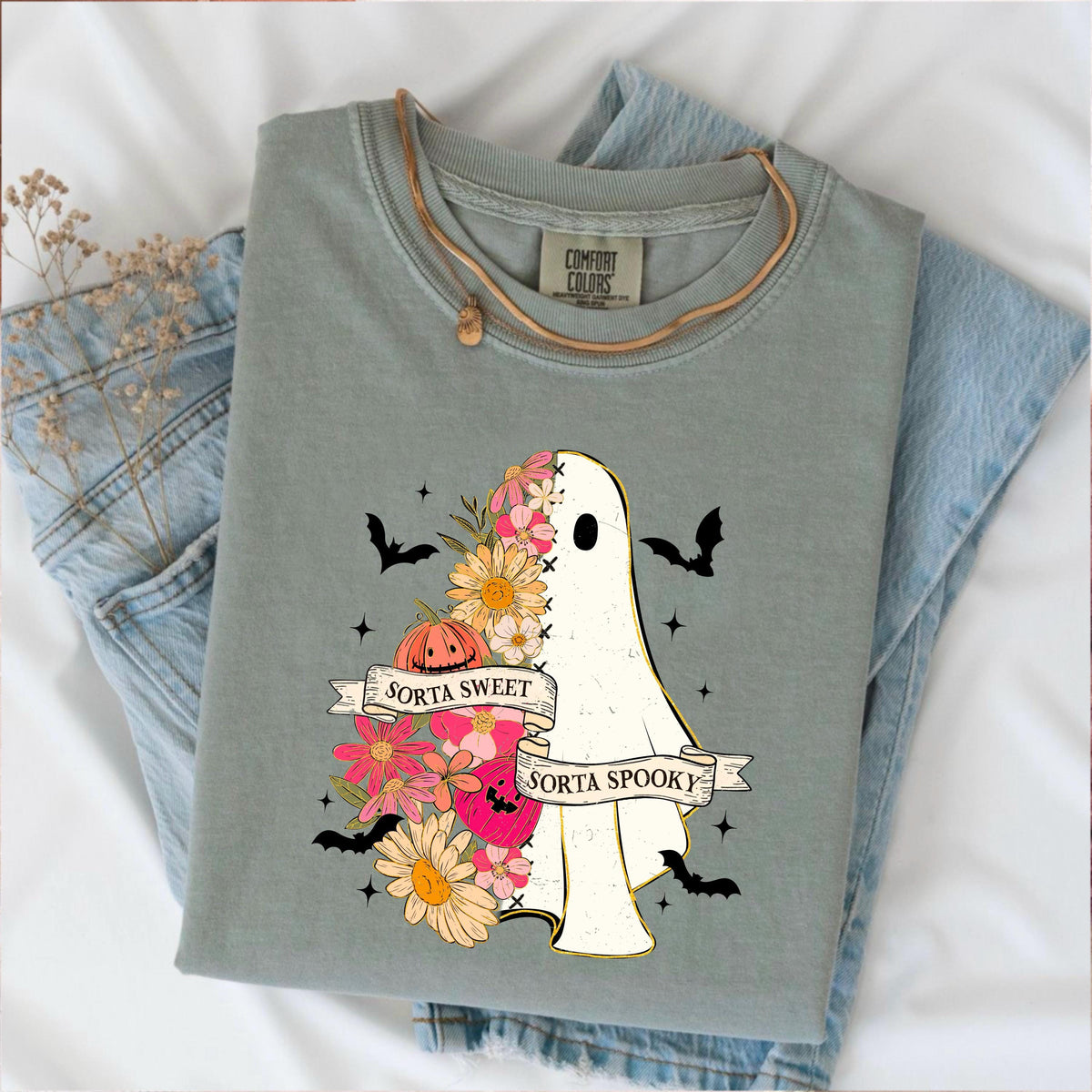 May include: Sage green Comfort Colors t-shirt featuring a ghost design. The ghost is half-floral and half-white, with the text "Sorta Sweet Sorta Spooky" on a banner. The design includes bats, a pumpkin, and flowers.