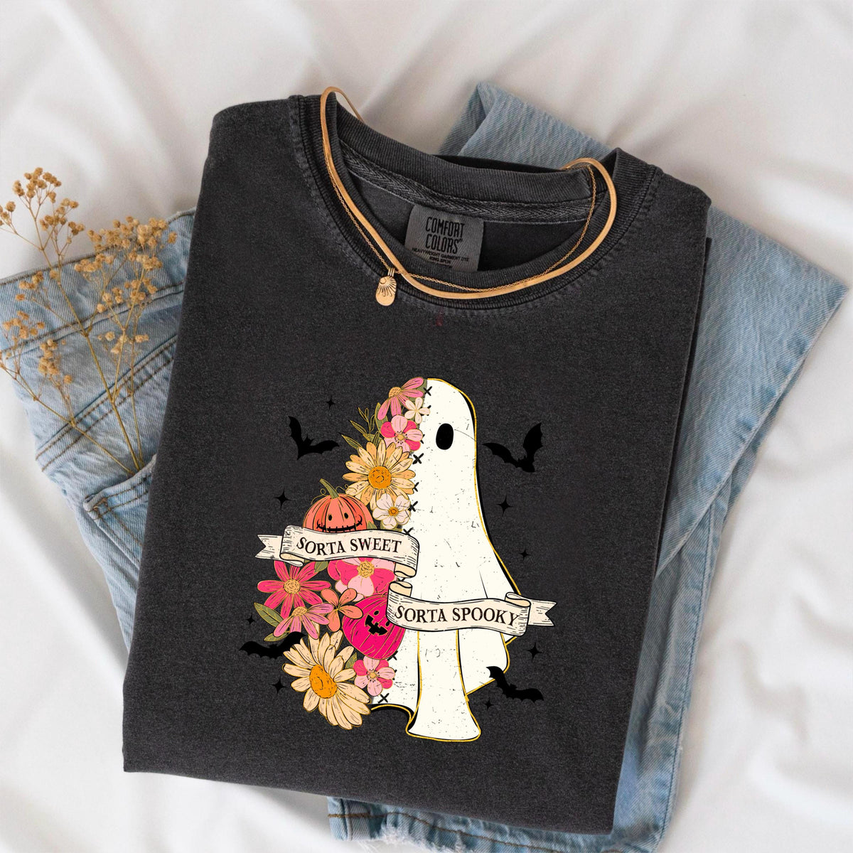 May include: Dark gray t-shirt with a ghost graphic. The ghost is decorated with flowers and a pumpkin, and the text reads "Sorta Sweet Sorta Spooky". A gold necklace is draped over the shirt.