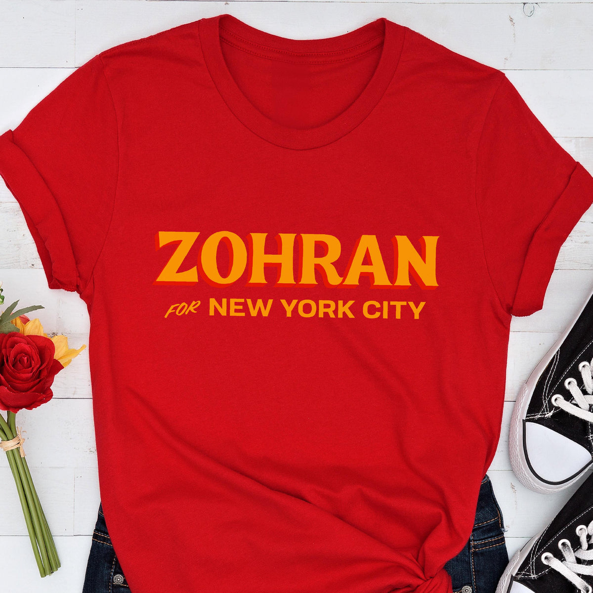 May include: A bright red short-sleeved t-shirt featuring the text ZOHRAN FOR NEW YORK CITY printed in bold yellow capital letters across the center of the chest. The shirt has a crew neckline and a standard fit with cuffed sleeves.
