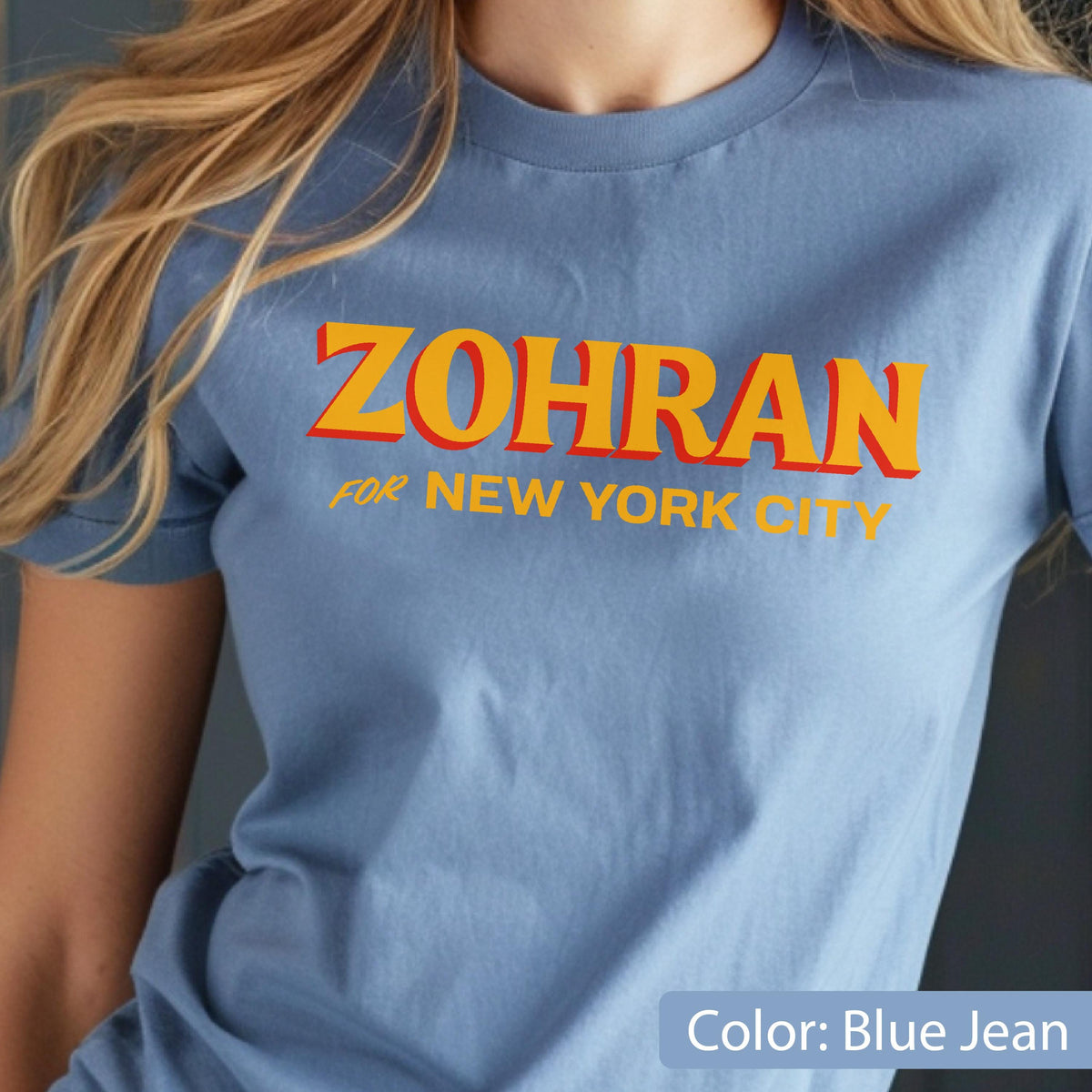 May include: A blue jean colored t-shirt with the word "ZOHRAN" in orange letters with a red outline, and the words "FOR NEW YORK CITY" in orange. The shirt is short-sleeved.