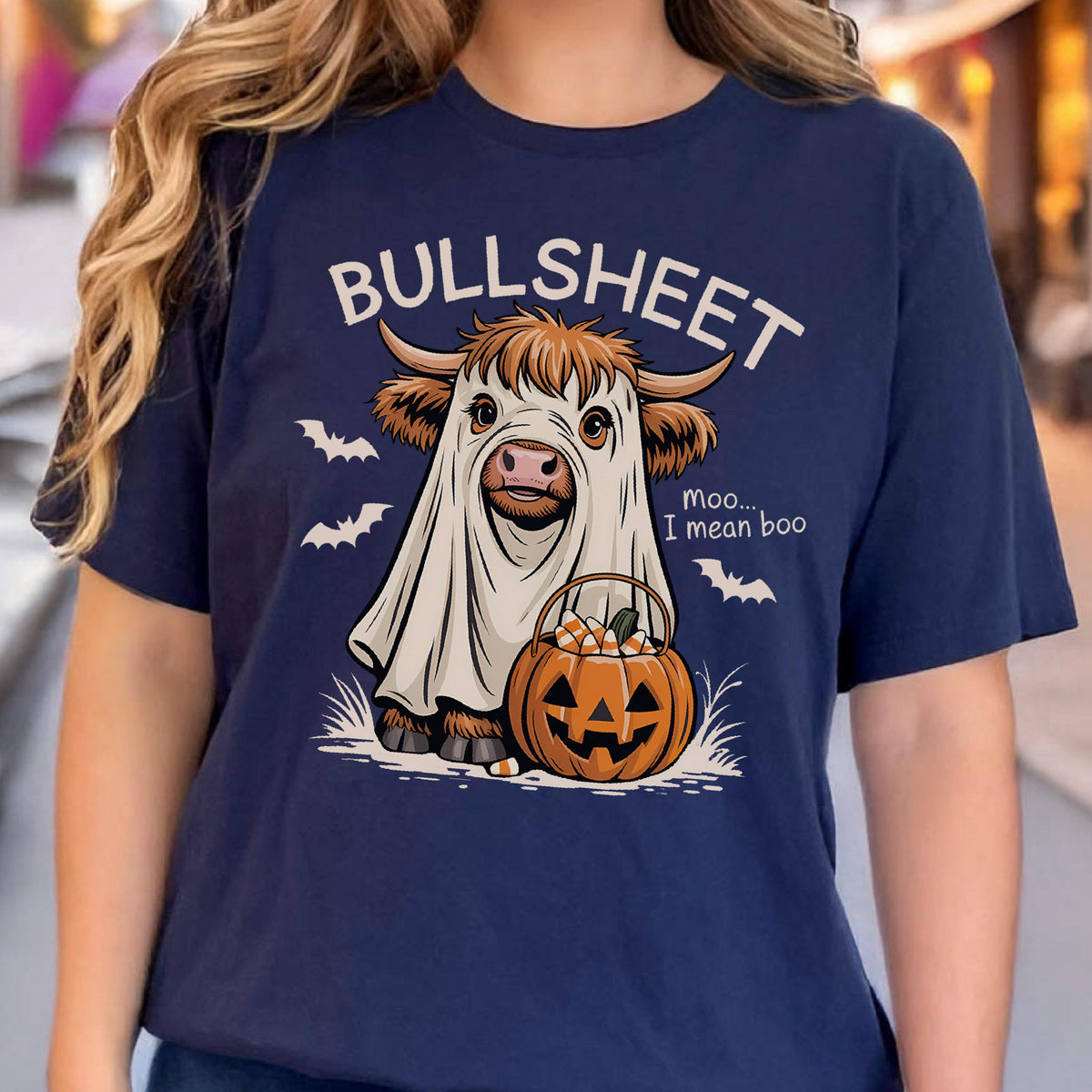 May include: Navy blue t-shirt with a Halloween-themed graphic. The design features a cow dressed as a ghost, a jack-o'-lantern, and the words "BULLSHEET" and "Moo... I mean boo." Bats are also included in the design.