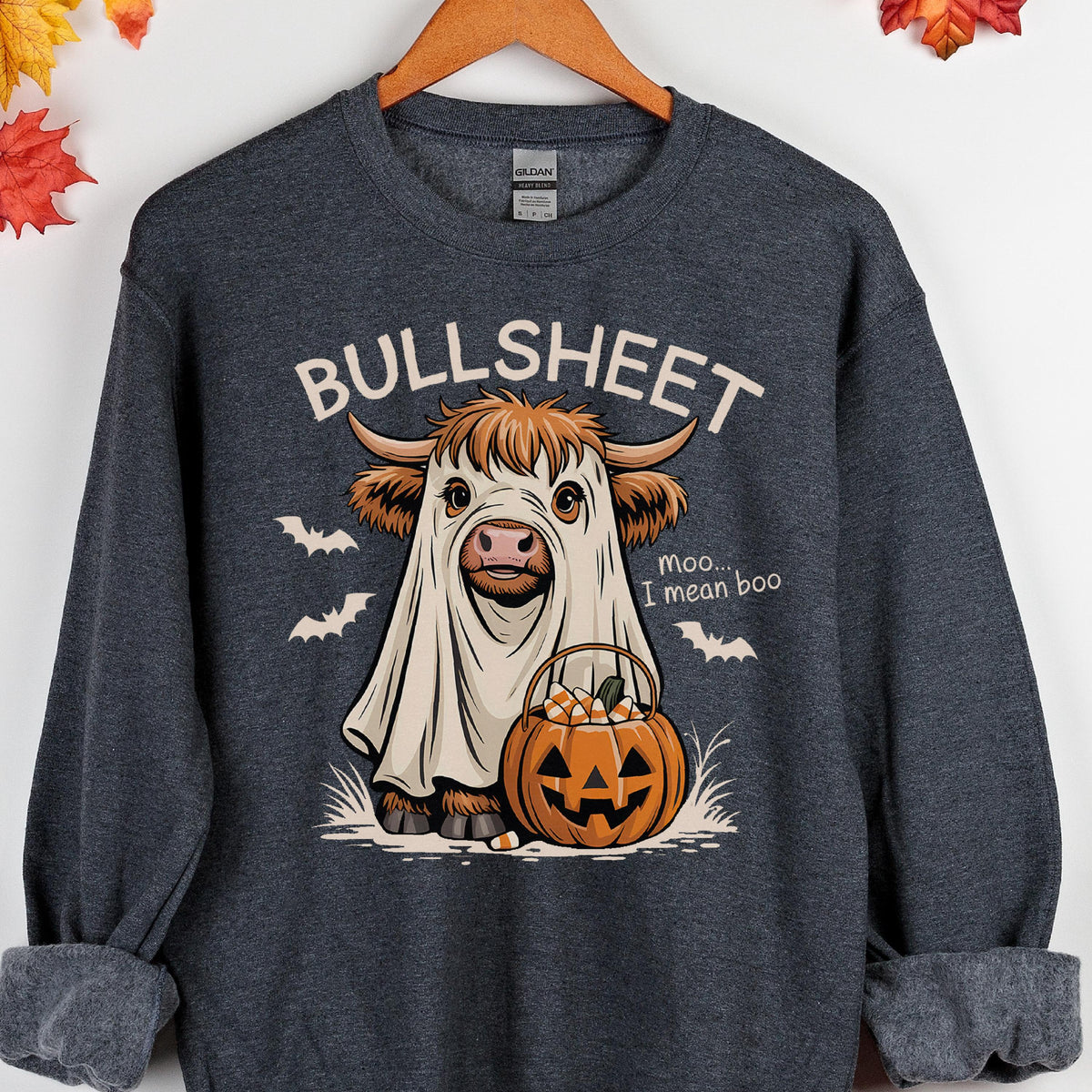 May include: Dark gray sweatshirt with a Halloween-themed graphic. The graphic features a cow dressed as a ghost with the word "BULLSHEET" above it. A jack-o'-lantern and bats are also included in the design. The text "Moo... I mean boo" is also present.