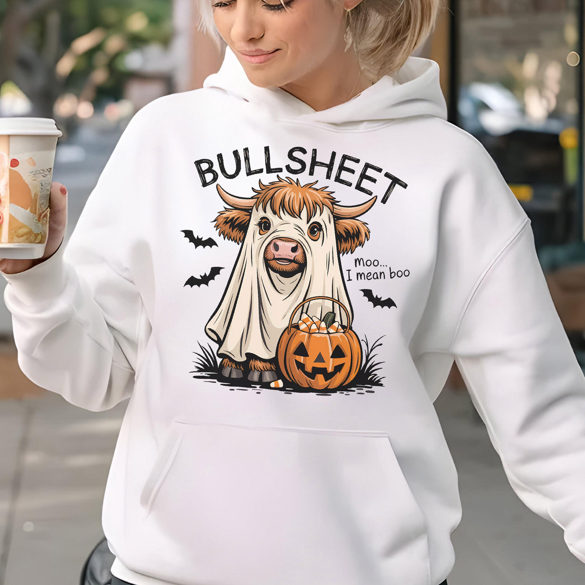 May include: White hoodie with a Halloween-themed graphic. The design features a cow in a ghost costume, a jack-o'-lantern, and the text "BULLSHEET" above the cow and "Moo... I mean boo" to the right. Black bats are also included.