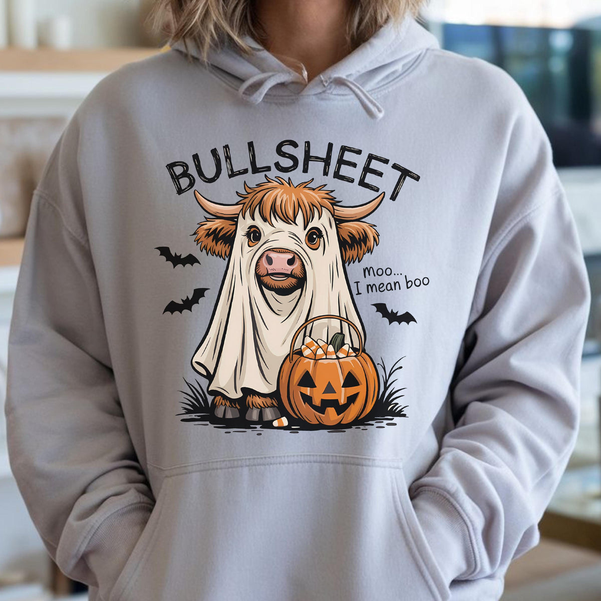 May include: A light gray hoodie featuring a Halloween-themed graphic. The graphic depicts a cow dressed as a ghost with the text "BULLSHEET" above and "Moo... I mean boo" next to it. A jack-o'-lantern and bats complete the design.