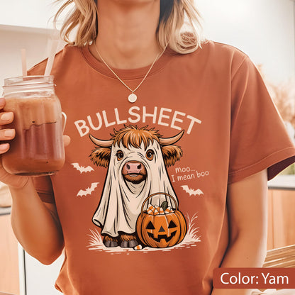 May include: A yam-colored t-shirt featuring a graphic of a Highland cow wearing a white ghost sheet, holding a jack-o'-lantern bucket filled with candy corn. The text reads BULLSHEET and moo... I mean boo, accompanied by small white bats.