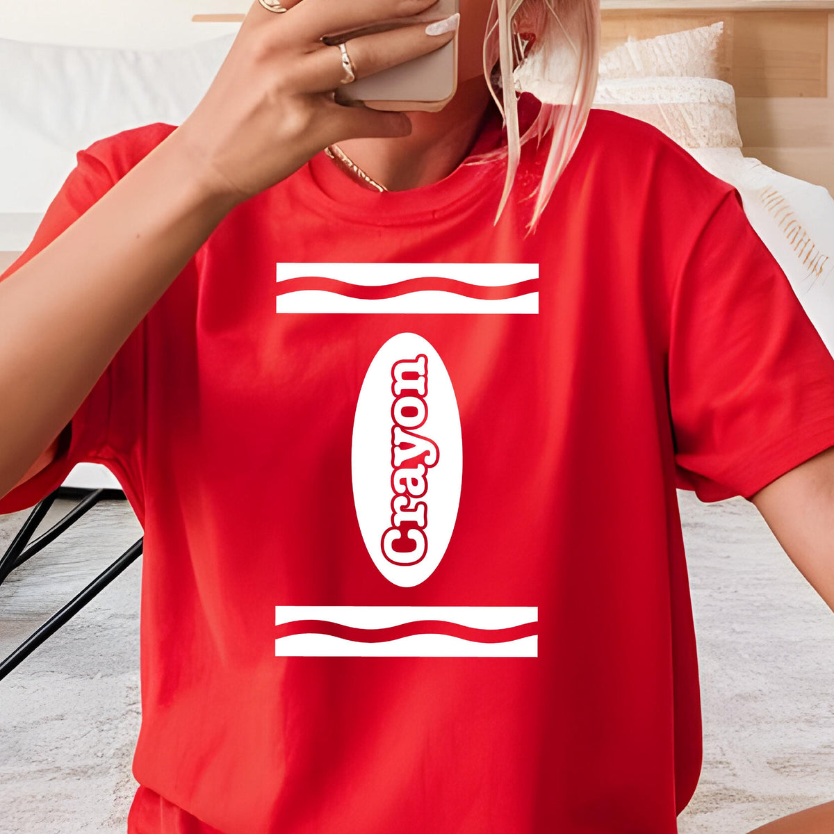 May include: A bright red short-sleeved t-shirt featuring a white graphic design that mimics a crayon wrapper. The design includes two horizontal wavy lines and a central vertical oval containing the word Crayon in white lettering.