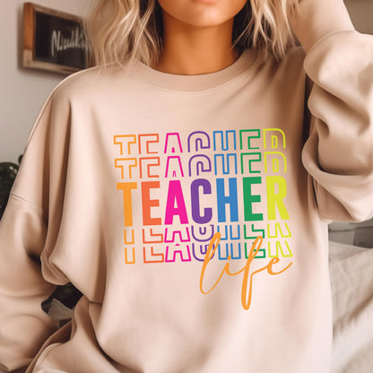 May include: A beige sweatshirt with the word "TEACHER" in large, colorful letters. The word "TEACHER" is stacked vertically, with the word "life" in cursive below. The sweatshirt is a neutral color.