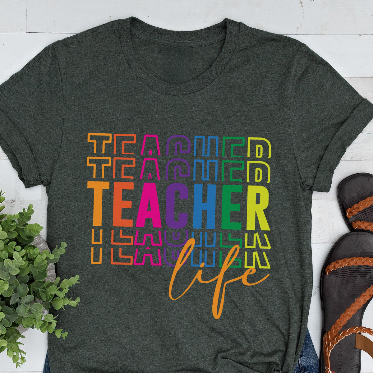 May include: Dark gray t-shirt with the words "TEACHER LIFE" in a colorful, stacked design. The word "TEACHER" is in a rainbow gradient, and "life" is in a cursive font. A casual, everyday tee.