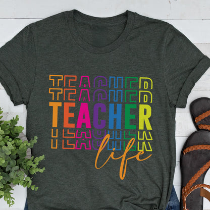 May include: Dark gray t-shirt with the words "TEACHER LIFE" in a colorful, stacked design. The word "TEACHER" is in a rainbow gradient, and "life" is in a cursive font. A casual, everyday tee.