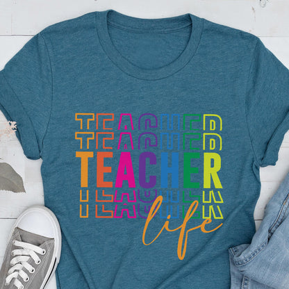 May include: Teal t-shirt with the word "TEACHER" in colorful stacked letters and the word "life" in cursive. A gray canvas sneaker is visible in the lower left corner. The shirt is made of a soft material.