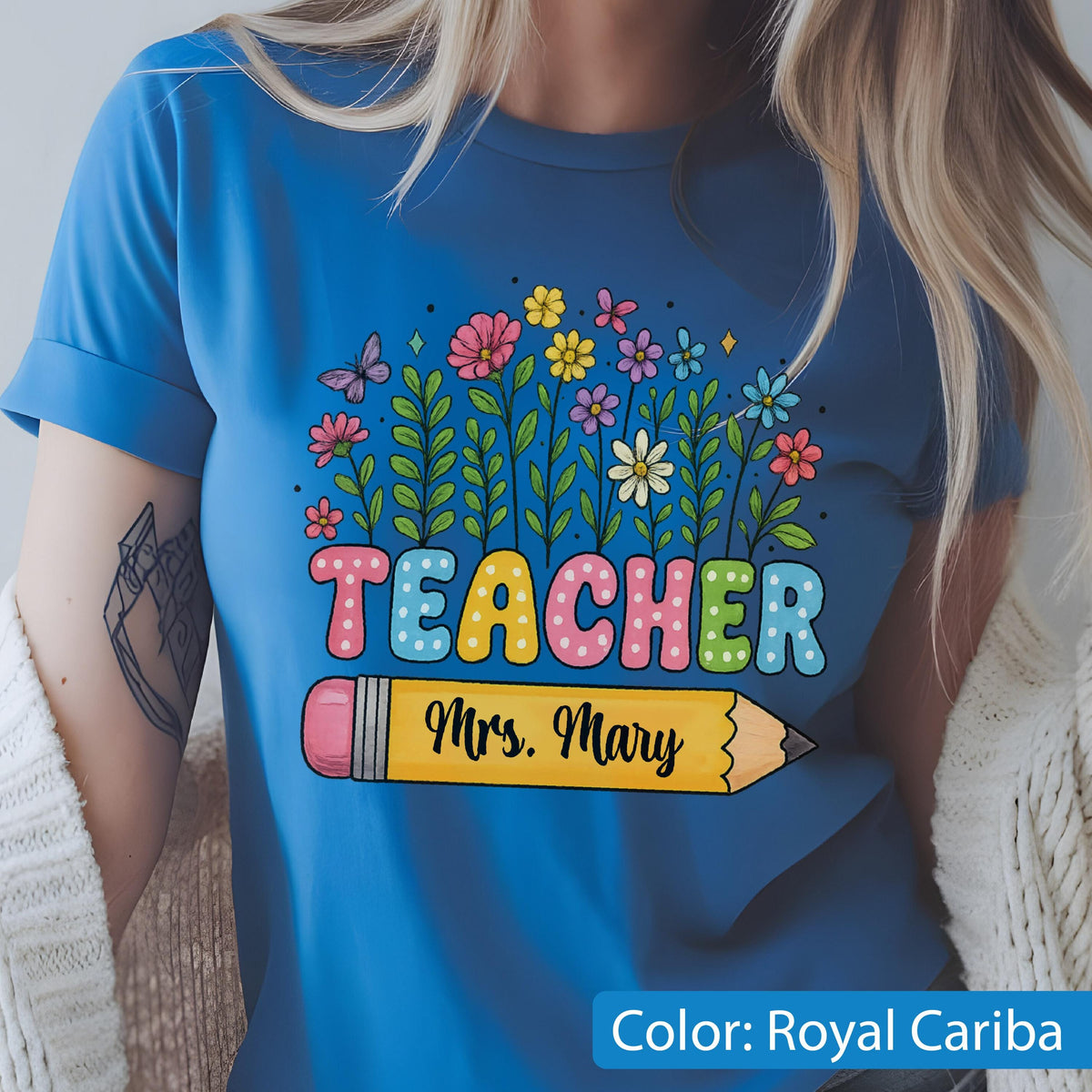 May include: Royal Cariba blue t-shirt with a colorful floral design and the word "TEACHER" in bubble letters. A yellow pencil with the name "Mrs. Mary" is below the word "TEACHER".
