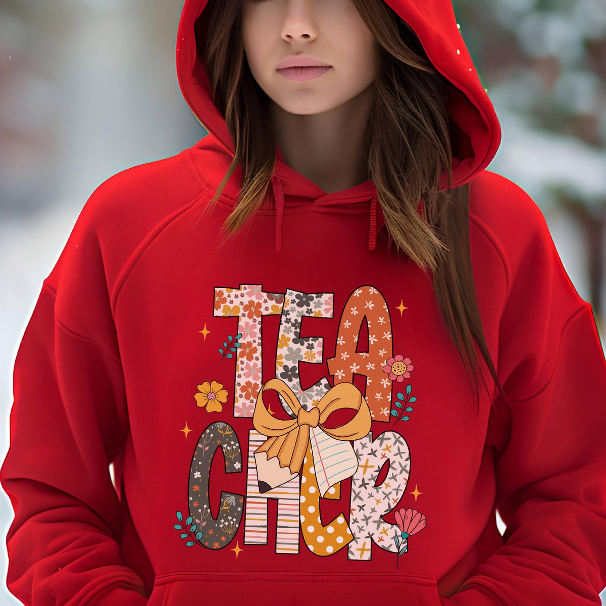 May include: A red hooded sweatshirt with the word "TEACHER" in a colorful floral and patterned design. The design includes a pencil, a bow, and floral accents. The sweatshirt is made of a soft material.