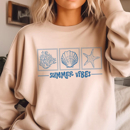 May include: Beige sweatshirt with a blue graphic of coral, a seashell, and a starfish in individual squares. The words "SUMMER VIBES" are written in blue below the images. The sweatshirt is a neutral color.