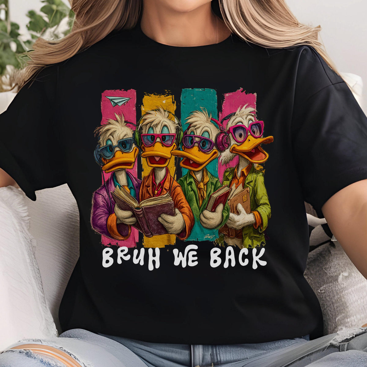 May include: Black t-shirt featuring a graphic of four cartoon ducks wearing glasses and reading books. The ducks are set against colorful vertical stripes. The text "BRUH WE BACK" is printed below the graphic.