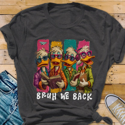 May include: Dark gray t-shirt featuring a cartoon illustration of four ducks wearing glasses and holding books. The ducks are set against colorful vertical stripes, with the text "BRUH WE BACK" in white.