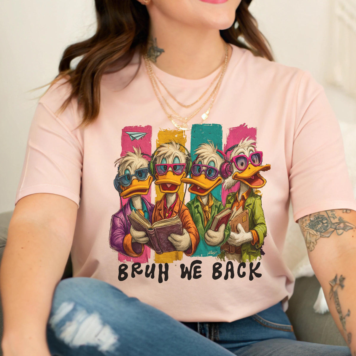 May include: A light pink t-shirt featuring a cartoon graphic of four ducks wearing glasses and holding books. The ducks are set against colorful vertical stripes, with the text "BRUH WE BACK" below the image.
