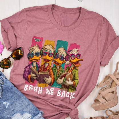 May include: A dusty rose t-shirt featuring a cartoon image of four ducks wearing glasses and headphones, each holding a book. The ducks are set against colorful vertical stripes. The text "BRUH WE BACK" is printed in white below the image.