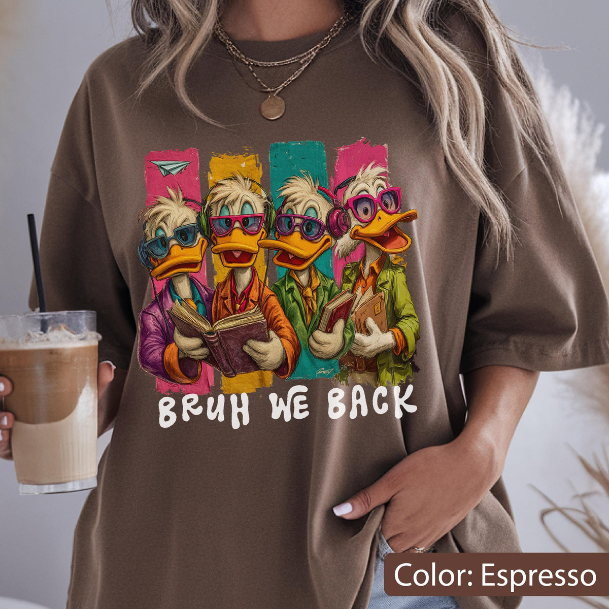 May include: Espresso-colored t-shirt featuring a graphic of four cartoon ducks wearing glasses and reading books. The ducks are set against colorful vertical stripes. The text "BRUH WE BACK" is printed below the ducks.