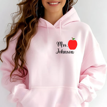 May include: Light pink hooded sweatshirt with the text "Mrs. Johnson" and a red apple graphic. The sweatshirt has a front pocket and a drawstring hood. The design is on the front of the sweatshirt.