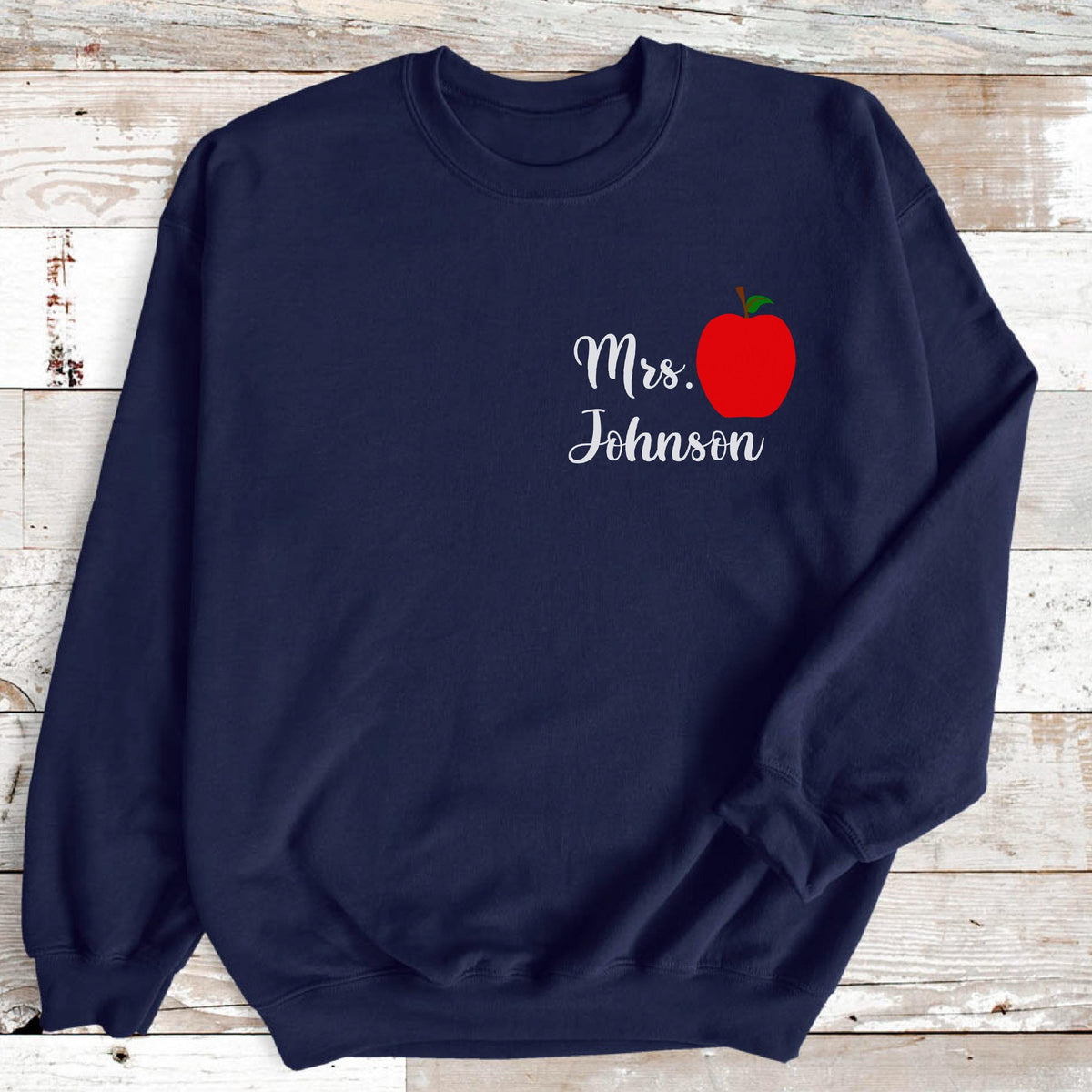 May include: Navy blue sweatshirt featuring the text "Mrs. Johnson" in a cursive font, accompanied by a red apple graphic with a green stem. The design is on the upper left chest area of the sweatshirt.
