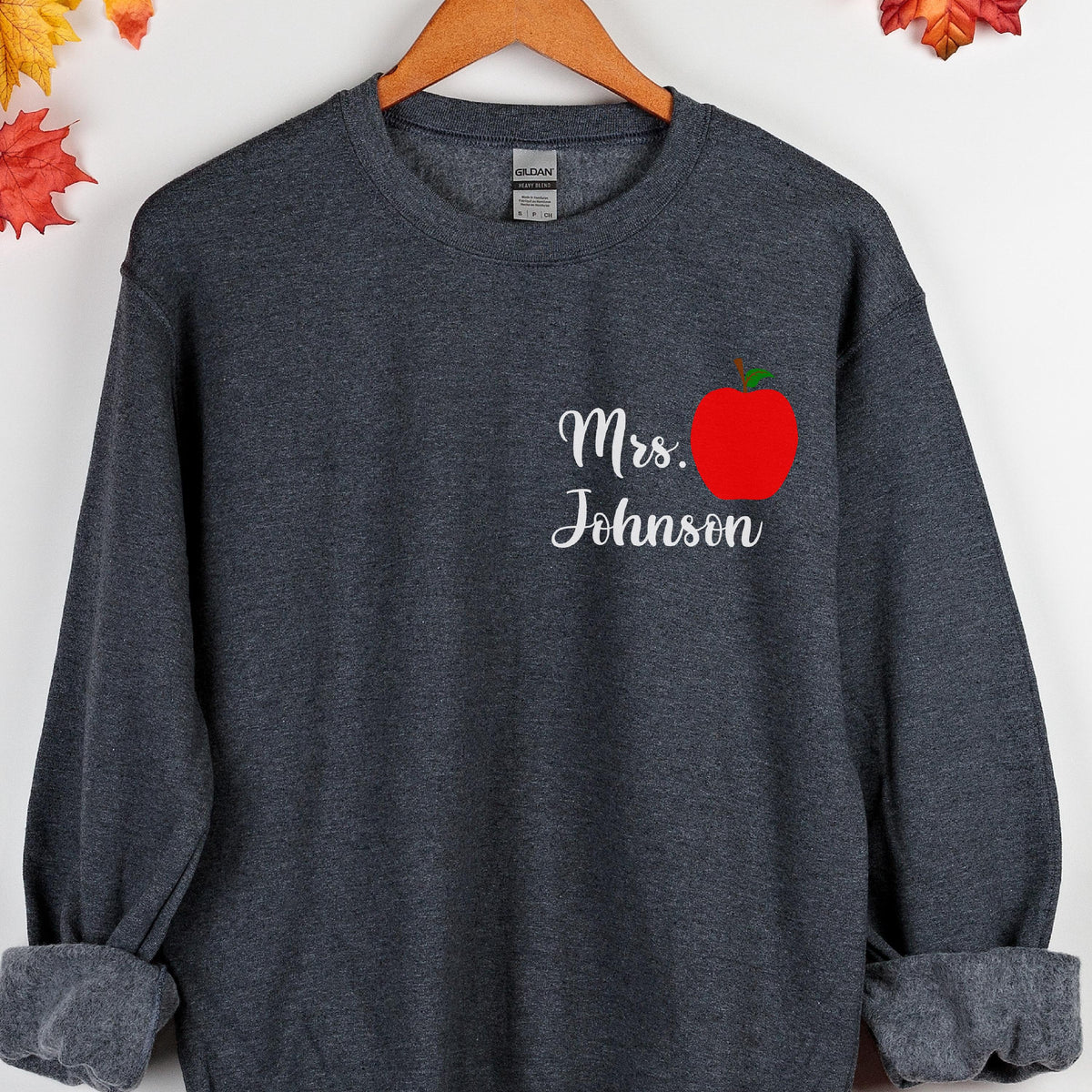 May include: Dark gray sweatshirt with the text "Mrs. Johnson" in white script and a red apple graphic. The sweatshirt has a crew neck and long sleeves, perfect for teachers.