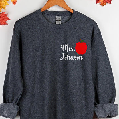 May include: Dark gray sweatshirt with the text "Mrs. Johnson" in white script and a red apple graphic. The sweatshirt has a crew neck and long sleeves, perfect for teachers.