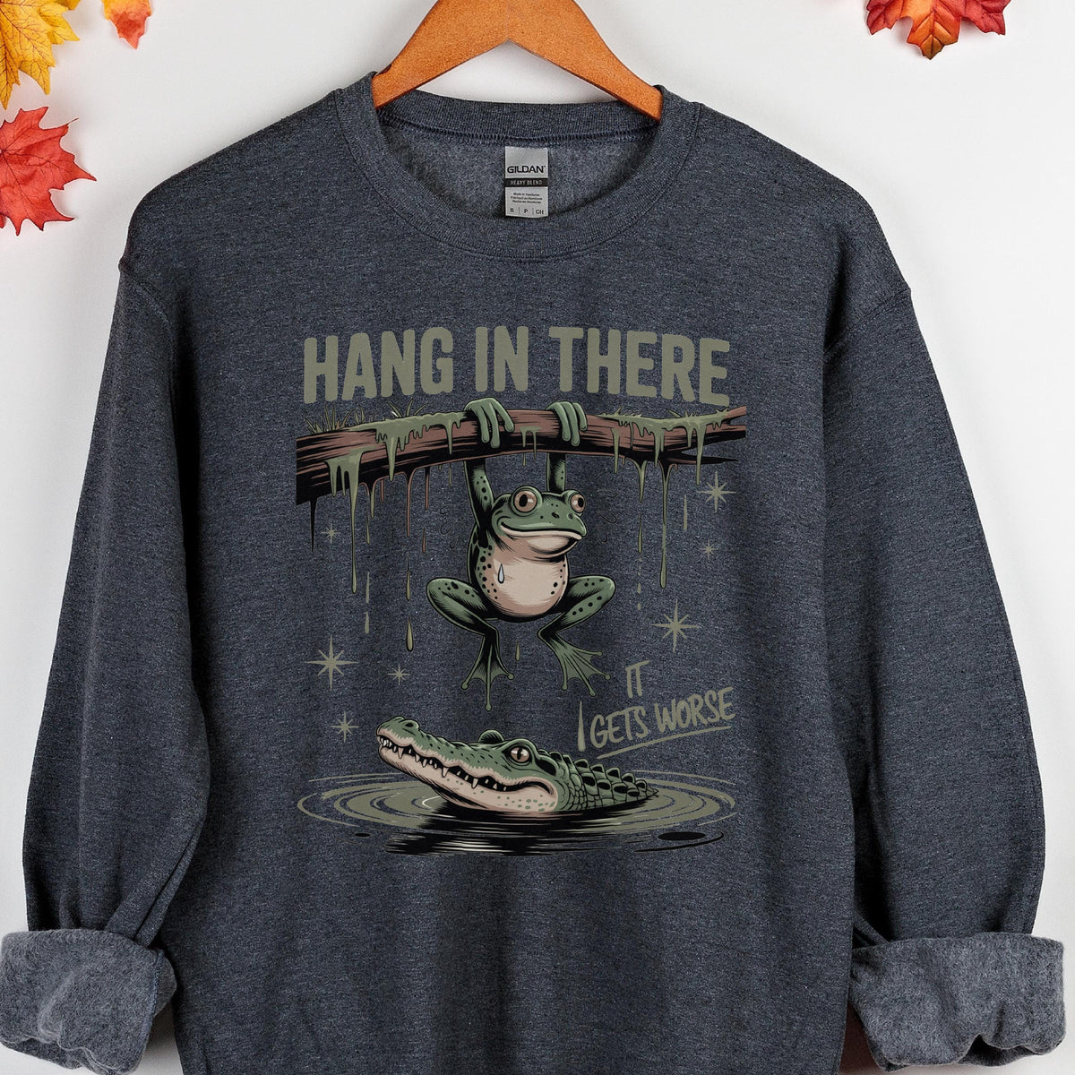 May include: Dark gray sweatshirt with a humorous graphic. The design features a frog hanging from a branch with the text "HANG IN THERE" above and an alligator below with the text "IT GETS WORSE".