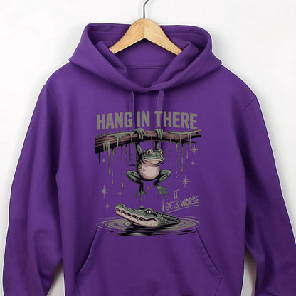 May include: A purple hoodie with a humorous graphic. The graphic features a frog hanging from a branch with the text "HANG IN THERE" above it. Below, an alligator lurks in the water, with the text "IT GETS WORSE".