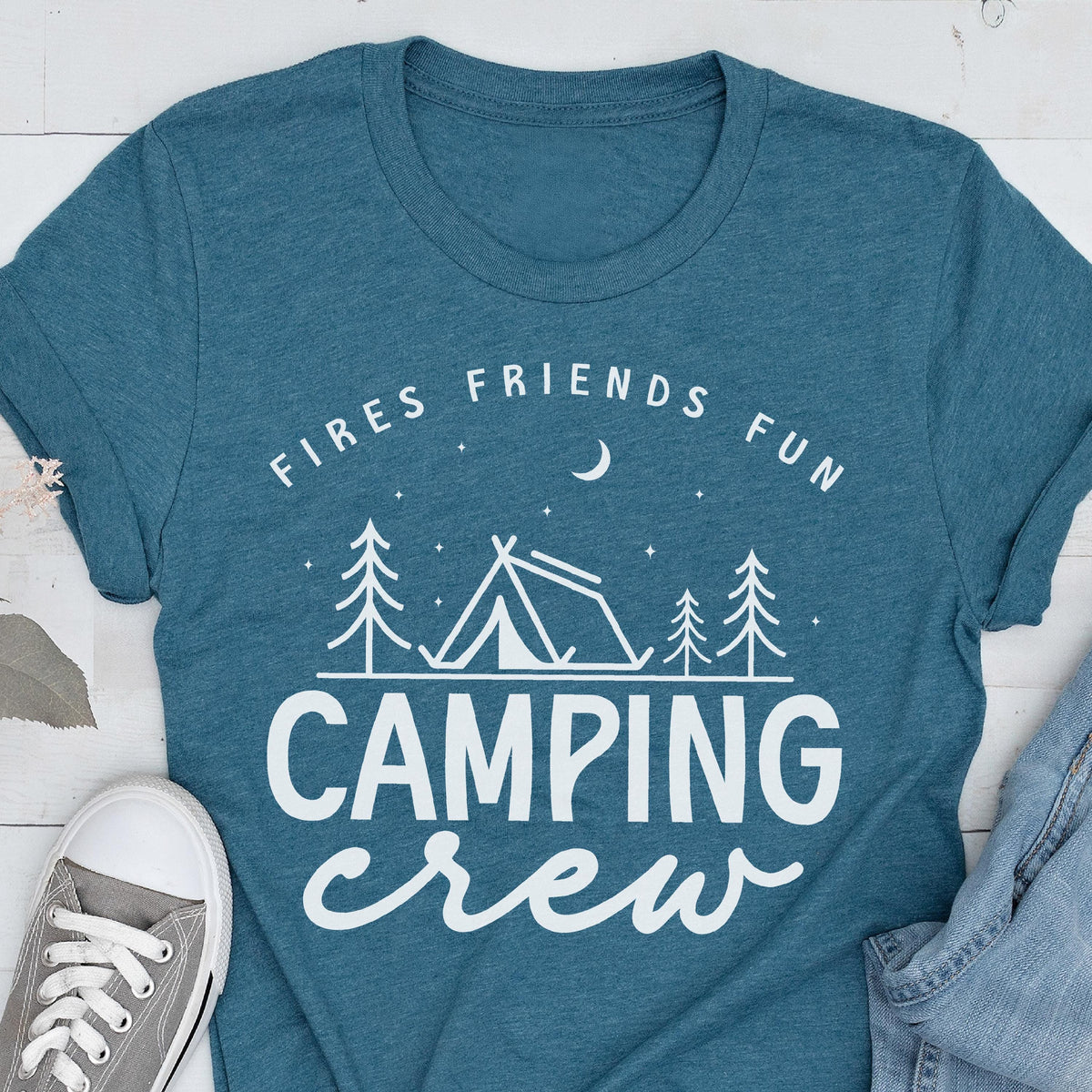 May include: Teal t-shirt with the words "Fires Friends Fun" above a camping scene with a tent and trees, and the words "Camping Crew" below. A gray sneaker and denim jeans are visible in the image.