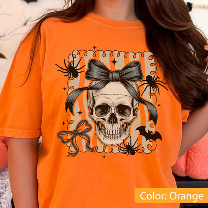 May include: Orange t-shirt featuring a skull with a black bow, spiders, and a bat graphic. The design is set within a decorative frame with stars. The text "Color: Orange" is at the bottom.