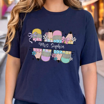 May include: Navy blue t-shirt featuring a colorful pencil design with the text "Mrs. Sophia". The pencils are decorated with bows and flowers. A cute and colorful design for teachers.