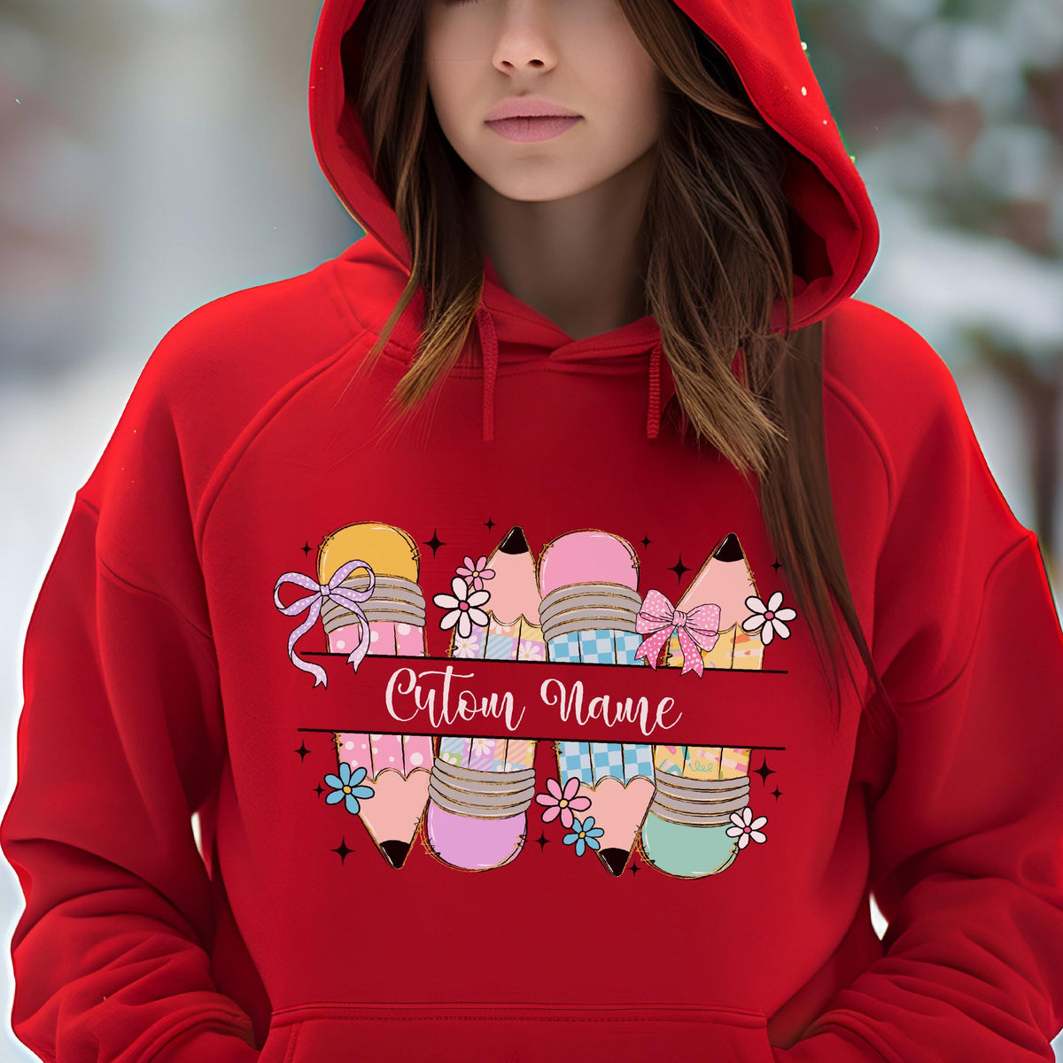 May include: Red hoodie featuring a colorful pencil design with bows and flowers. The design includes the text "Custom Name" in a cursive font. The pencils are in various colors, including yellow, pink, and blue.