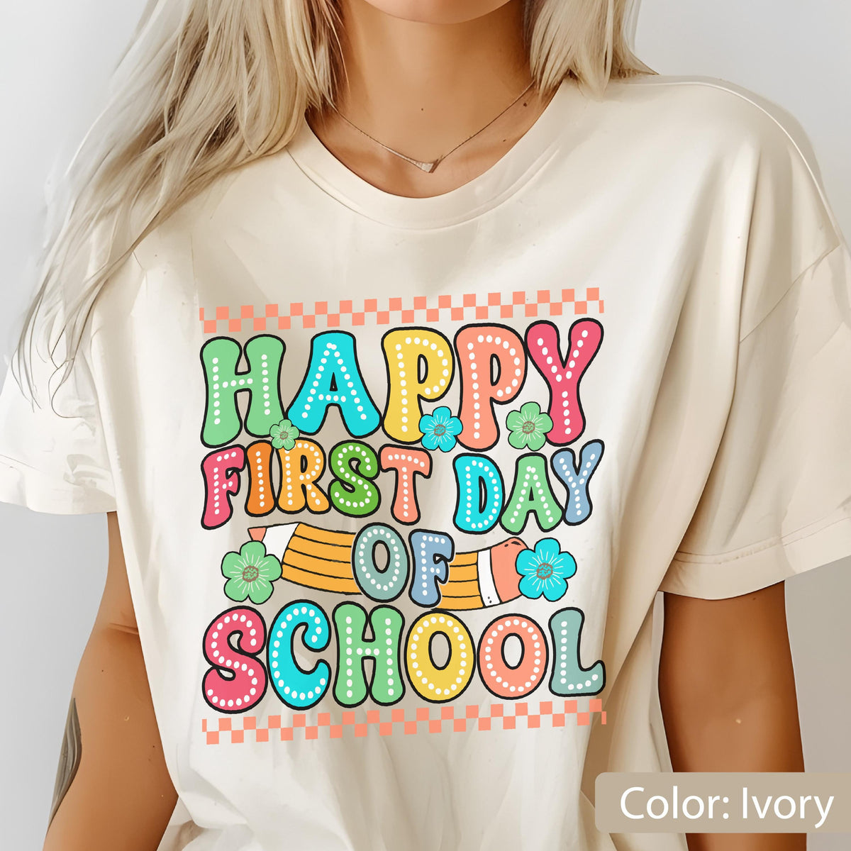 May include: An ivory t-shirt featuring a colorful graphic with the text "HAPPY FIRST DAY OF SCHOOL" in a retro, bubbly font. The design includes a yellow pencil illustration, small blue and green flowers, and orange checkered borders at the top and bottom.