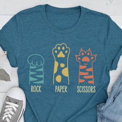 May include: A heathered teal short-sleeve t-shirt featuring a graphic of three animal paws. The first paw is light blue with stripes labeled ROCK, the second is yellow with spots labeled PAPER, and the third is orange with stripes labeled SCISSORS.