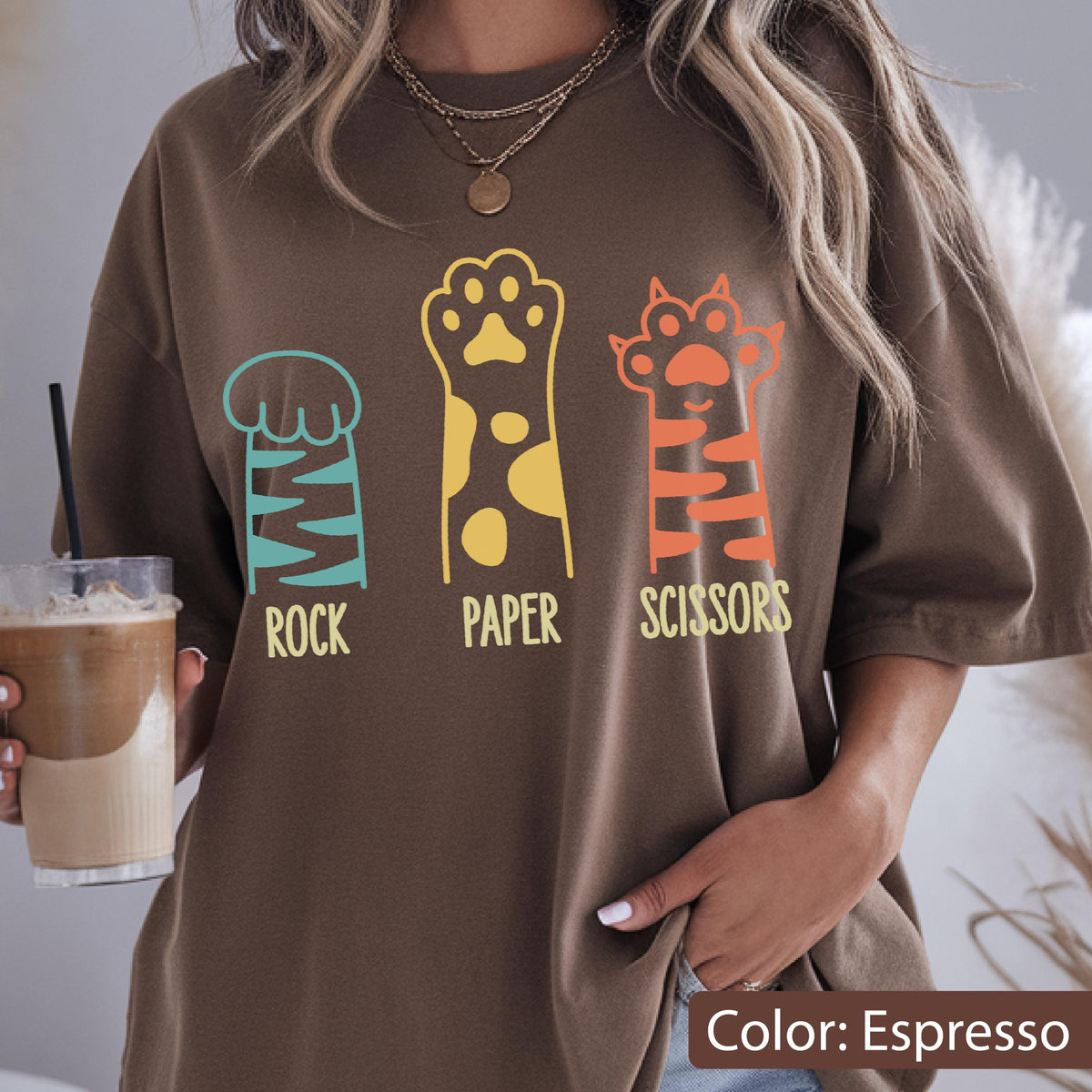 May include: An espresso brown t-shirt featuring a graphic print of three animal paws. The first paw is teal with the word ROCK, the second is yellow with spots and the word PAPER, and the third is orange with stripes and the word SCISSORS.