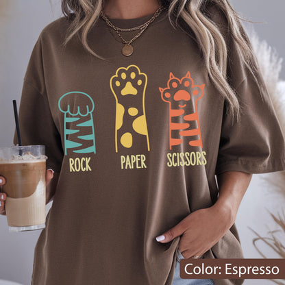 May include: An espresso brown t-shirt featuring a graphic print of three animal paws. The first paw is teal with the word ROCK, the second is yellow with spots and the word PAPER, and the third is orange with stripes and the word SCISSORS.