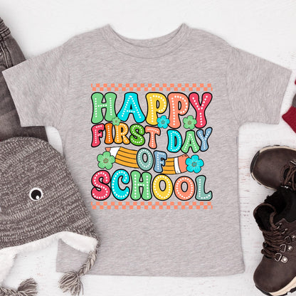 May include: A heather gray t-shirt featuring a colorful graphic with the text Happy First Day Of School in a bubble font. The design includes a yellow pencil, small teal flowers, and an orange checkered border at the top and bottom edges.