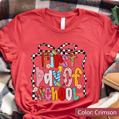 May include: Crimson-colored t-shirt with a colorful graphic that reads "First Day of School." The text is designed with various patterns and colors, including stars, flowers, and lightning bolts. A black and white checkered ribbon frames the text.