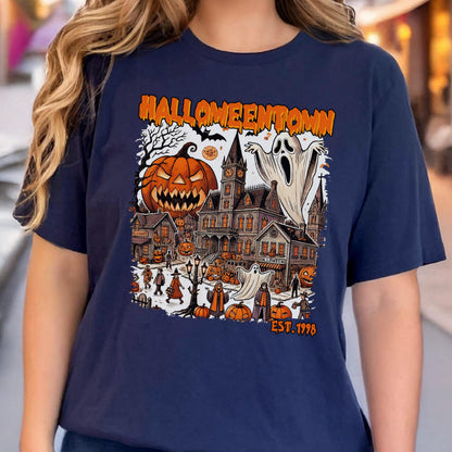 May include: Navy blue t-shirt featuring a Halloween-themed graphic. The design includes a jack-o'-lantern, a haunted house, ghosts, and the text "Halloweentown EST. 1998". The graphic is in shades of orange, white, and black.