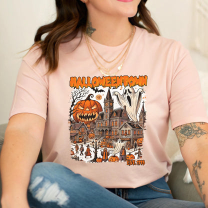 May include: Pink t-shirt featuring a Halloween-themed graphic. The design includes a jack-o'-lantern, a haunted house, ghosts, and the text "Halloweentown EST. 1998". The graphic is in shades of orange, black, and white.