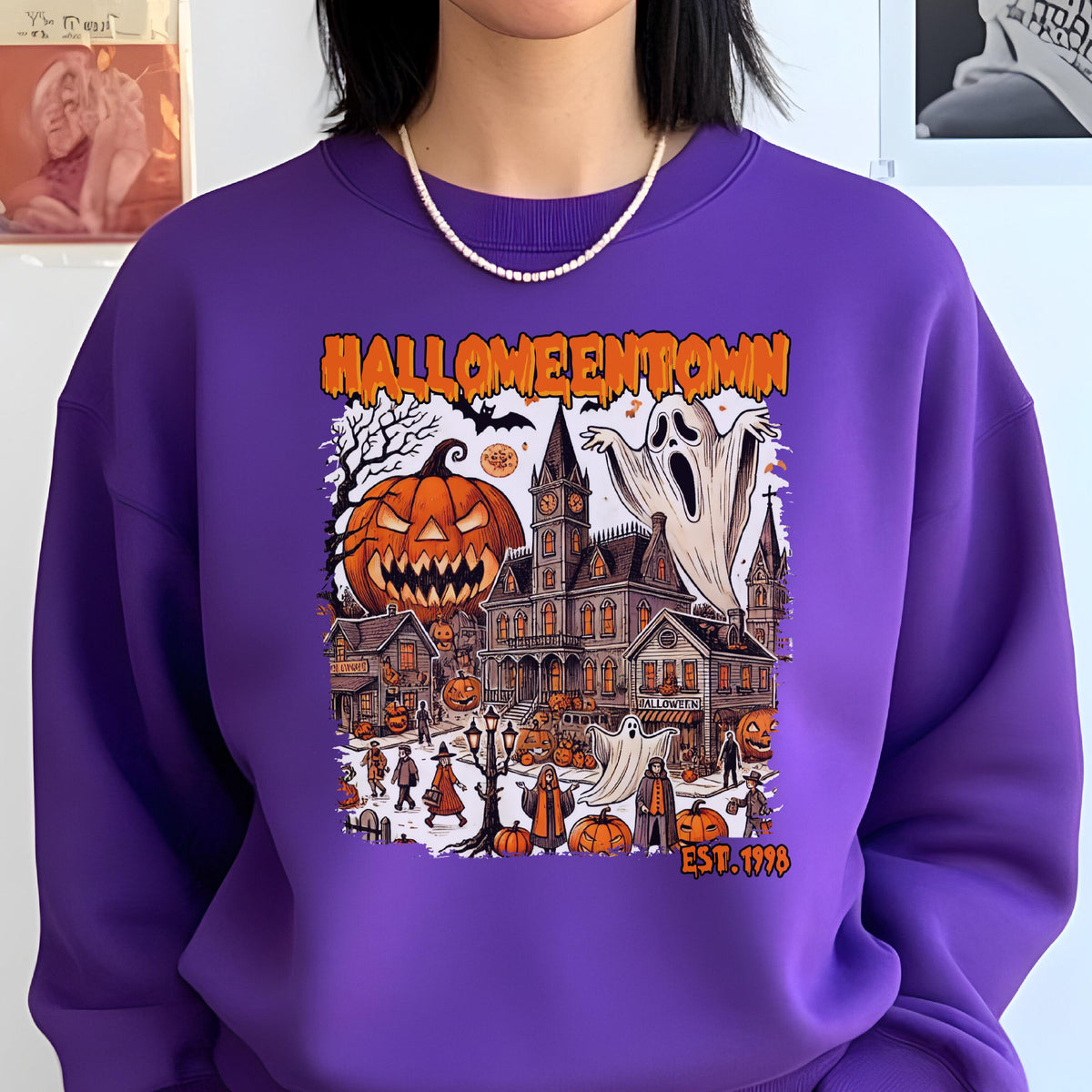 May include: A purple crewneck sweatshirt featuring a graphic print with the text HALLOWEENTOWN EST. 1998. The design depicts a spooky town scene with a large jack-o'-lantern, a tall clock tower, ghosts, and various figures in a Halloween setting.