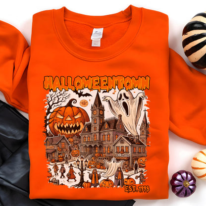 May include: An orange crewneck sweatshirt featuring a graphic print with the text HALLOWEENTOWN and EST. 1998. The illustration depicts a spooky town scene with a large jack-o'-lantern, a haunted mansion, ghosts, and various figures in costumes.