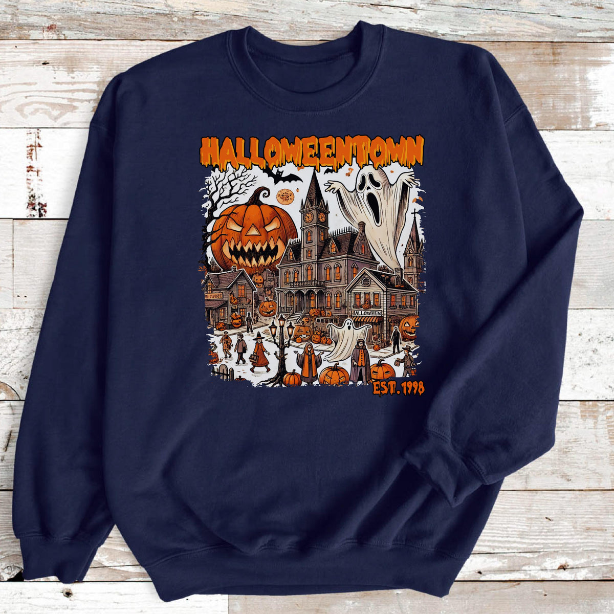 May include: A navy blue crewneck sweatshirt featuring a graphic print with the text HALLOWEENTOWN EST. 1998. The design depicts a spooky town scene with a large jack-o'-lantern, a ghost, a tall building, and various smaller pumpkins and figures.