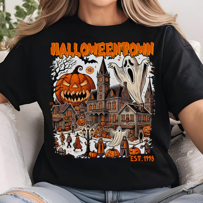 May include: Black t-shirt featuring a Halloween-themed graphic. The design includes a jack-o'-lantern, a haunted house, ghosts, and the text "Halloweentown EST. 1998" in orange. The artwork has a vintage, cartoonish style.